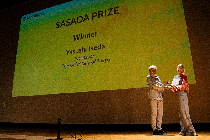 　CAADRIA 2026におけるSasada Prize授賞式：左は受賞者の池田靖史氏、
　右はSasada Prize委員会委員長の Christiane Herr 南方科技大学教授